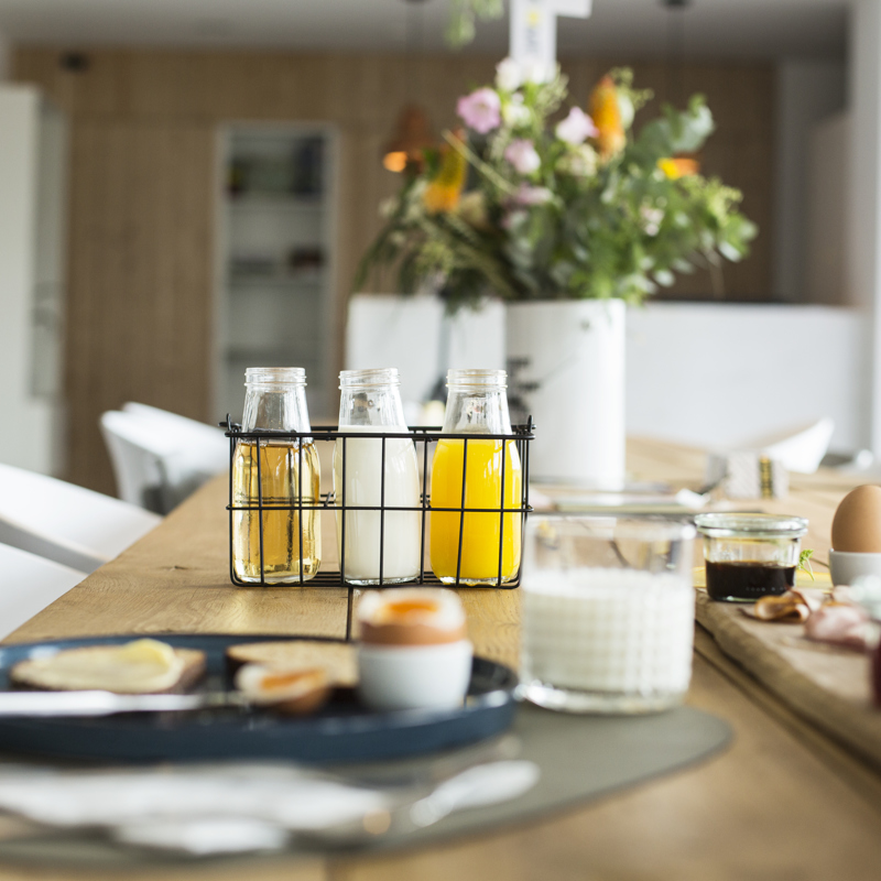 Gedekte ontbijttafel met vers sap, een eitje, glas melk en een houten plank met smeersels. 