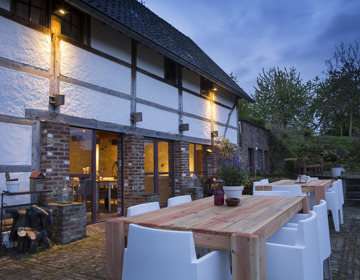 Groot terras met witte stoelen en houten tafels bij schemering.