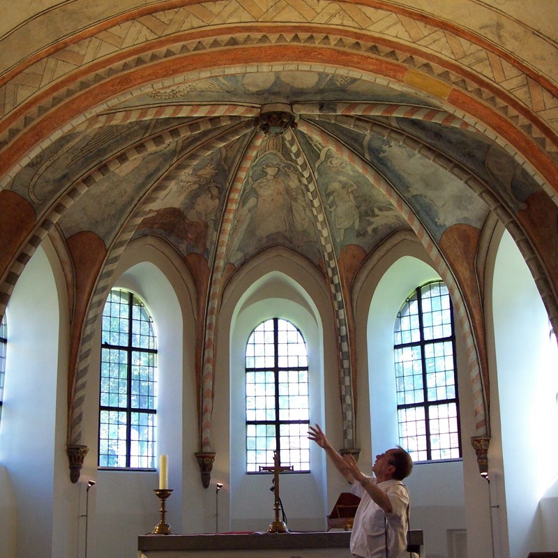 Een pastoor maakt een dramatisch gebaar naar de muurschilderingen in de koepel van het Salvius Kerkje