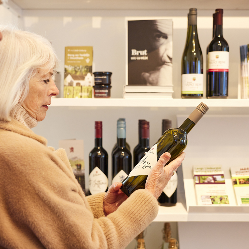 Een oudere vrouw die naar een fles wijn kijkt